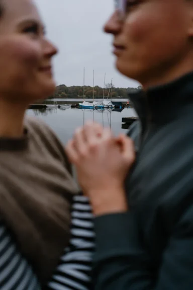 Paar hält sich am Hafen an den Händen, im Hintergrund liegen Boote.