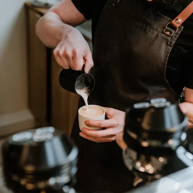 Brand Shooting Barista in Münster Barista gießt Milch in eine Tasse für einen Kaffee.