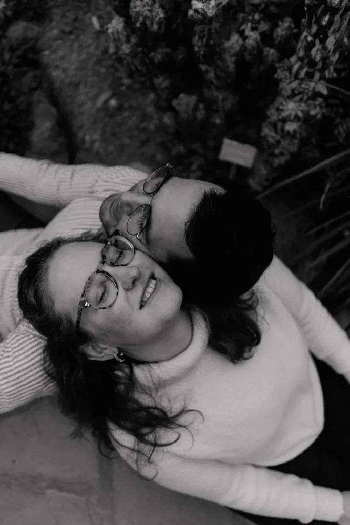 Paarshooting im botanischen Garten in Münster Lächelndes Paar in Umarmung, umgeben von Pflanzen, in Schwarz-Weiß.