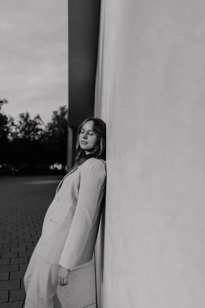 Portraitshooting in Münster am LWL Museum Junge Frau in Anzug lehnt entspannt gegen eine Wand, mit einem nachdenklichen Ausdruck.
